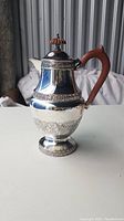 Silver plated coffee pot with engraved Aganthus pattern and wooden handle on white surface