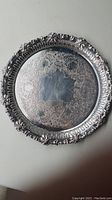 Top-down view of medium round silver plate serving tray showing detailed engraved surface and acorn and leaves trim around the edge.