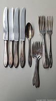 Photo of silver plate silverware set consisting of 4 dinner knives, 4 dinner forks, 4 dessert forks, and 1 spoon all engraved with the initial 'G'. Pieces show some tarnishing but are in good condition overall.