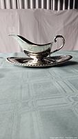 Side view of silver plated gravy boat on matching serving tray, showing profile and handle design.