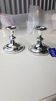 Pair of silver plated candlestick holders on white surface with protective wrapping in the background.