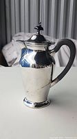 Front view of the Victorian silver plate coffee pot with black handle showing reflective surface and slight tarnish.