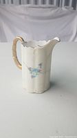 Front view of the vintage cream jug showing blue floral artwork and gold handle