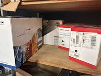 Four boxes of new laser toner cartridges including Xerox and Office Depot brands, stacked on wooden shelves.