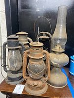 Group of 5 antique railroad lanterns and oil lamp arranged on table showing rust and dust.