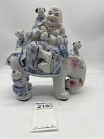 Front and side views of ceramic Happy Buddha figurine sitting on a decorated elephant with five children figures around it