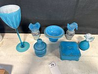 Wide view of six blue glass items showing various shapes and gold/silver accents.