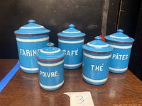 Five blue enamel nesting canisters with French labels, on wooden surface against dark background.