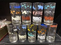 Set of 9 mid-century drinking glasses with cityscape designs and city names from Singapore, London, Rome, New York, Istanbul, and Paris arranged on a shelf.