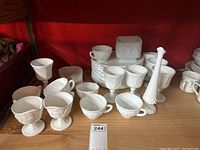 Wide view of milk glass lot including goblets, cups, dishes stacked, and decorative containers against a red background