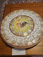 Top view showing the circular mosaic tile lazy Susan with a rooster in the center and colorful border details, resting on a wooden table.