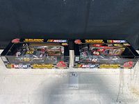 Photo showing both NASCAR 1:64 scale transporter toys in original packaging, side by side on a surface.