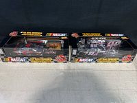 Two NASCAR 1:64 scale transporter toy trucks in original packaging, side view.