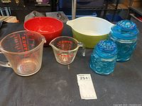 Full view of the lot including green and red Pyrex bowls, two Pyrex measuring cups, and two blue glass canister jars with lids