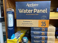 Stack of five Aprilaire Water Panel Evaporator Humidifier Filter boxes, model 35, next to two EveryDrop refrigerator water filters in plastic packaging, and one yellow boxed 6-outlet power strip.