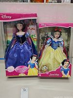 Two boxed Snow White porcelain dolls, one in classic yellow and blue dress, the other in purple gown.