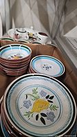 Stack of hand-painted ceramic dishes including dinner plates and salad plates showing floral and bird designs.
