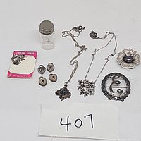 Full view of all jewelry items and container tube arranged on white surface showing chains, brooches, lockets and earrings.