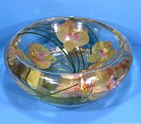 Side angle showing detailed embedded orchid flowers and green stems inside clear glass bowl.
