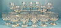 Front view of all 15 glasses in the set, showing size variation and textured thistle pattern