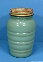 Full view of the pepper shaker showing opaque pale green ribbed glass body and metal lid with floral tulip design.
