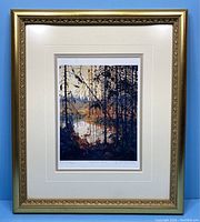 Framed artwork showing the full gold ornate frame and matting around the lithograph of river through trees.