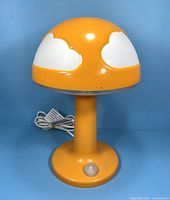 Front side view of orange and white Ikea Skojig mushroom cloud desk lamp with visible power cord and switch on base.
