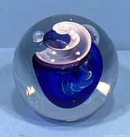 Front view of the clear round glass paperweight showing the inner cobalt blue and white swirl pattern with embedded air bubbles.