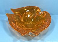 Front angled view of the vintage Chalet art glass bowl showing its bright orange color and flowing curves.