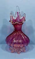 Front view of cranberry blown glass vase with ruffled top and star base.