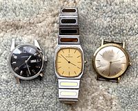Three vintage men's wristwatches including Eterna with metal band, Caravelle and Timex without bands laid side by side on carpeted surface.