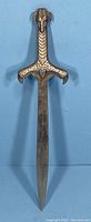 Full length view of vintage metal letter opener with dragon head handle on blue background.