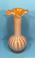 Front view of the peach and white striped Murano blown glass vase with ruffled top, set against blue background.