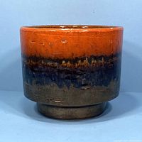 Front view of vintage West German planter showing orange, blue and brown glazing with textured surface marks.