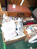 Overview of wooden box on top of cardboard box showing contents including paint tubes and solvent bottle