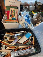 Overall view of black plastic bin containing brushes, pencils, ruler and white storage bins behind