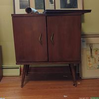 Front view of the wooden record cabinet showing two doors and angled bronze-colored handles on four tapered legs.