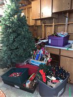 Wide view showing artificial Christmas tree, multiple bins of Christmas ornaments, wrapping paper, basket of bows and lights