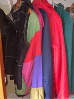 Several coats including a vintage green wool angora blend, colorful patchwork coat, red and blue puffer jackets, teal London Fog coat, and black vest.