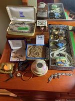 Overview of lot showing jewelry pieces including necklaces, bracelets, earrings, hair jar, compact, and jewelry boxes arranged on a dresser surface.