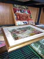 Framed oil painting of antique buffet with decorative items and chair behind, wooden frame
