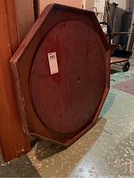 Front and angled views of an octagonal wooden crokinole game board with marked scoring rings and some surface stains.