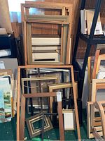 Various wooden frames stacked against a wall, showing different sizes and finishes with some painted and some natural wood