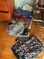 Overview of all items including sweaters, scarves, shoes, suitcase, handbag and boxed bras, laid on the floor and in a bin