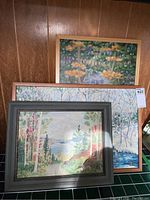 Three framed paintings stacked, showing the variety in size and scenes including floral and forest landscapes.