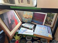Shelf display showing multiple original artworks by Mary E Crawford, various sizes and styles, some framed, some unframed