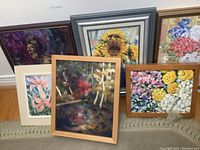 Photo showing six original acrylic paintings by ME Crawford, featuring floral themes and one portrait, arranged leaning against a wall and on a rug.