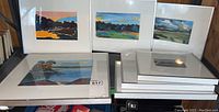 Photo showing six framed landscape artworks by Mary C Crawford, various sizes, arranged on a surface, all with silver metal frames and white mats.