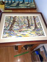 Photo of framed oil painting showing light and shadow on trees with multicolor brushstrokes on canvas or board.