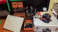 Overview photo showing multiple vintage cameras, carrying cases, and accessories including silver hard case and flash unit.